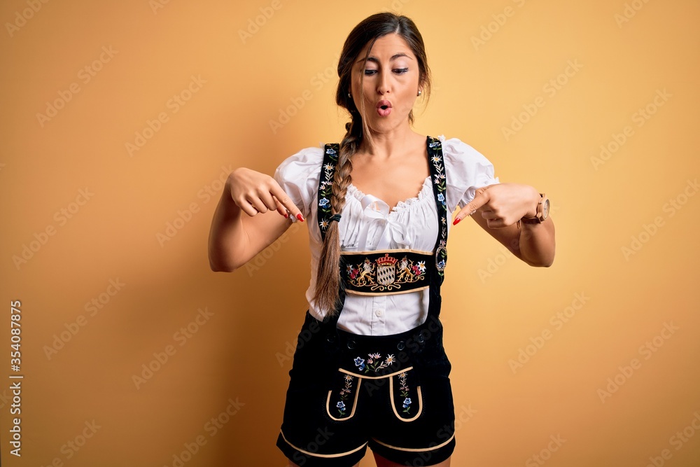Young beautiful brunette german woman celebrating Octoberfest wearing traditional dress Pointing down with fingers showing advertisement, surprised face and open mouth Young beautiful brunette german woman celebrating Octoberfest wearing traditional dress Pointing down with fingers showing advertisement, surprised face and open mouth