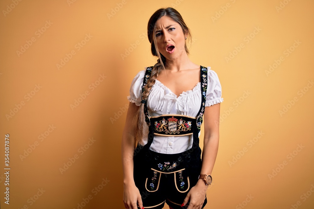 Young beautiful brunette german woman celebrating Octoberfest wearing traditional dress In shock face, looking skeptical and sarcastic, surprised with open mouth Young beautiful brunette german woman celebrating Octoberfest wearing traditional dress In shock face, looking skeptical and sarcastic, surprised with open mouth