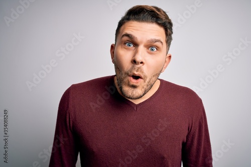 Young man with blue eyes wearing casual sweater standing over isolated background afraid and shocked with surprise expression, fear and excited face.