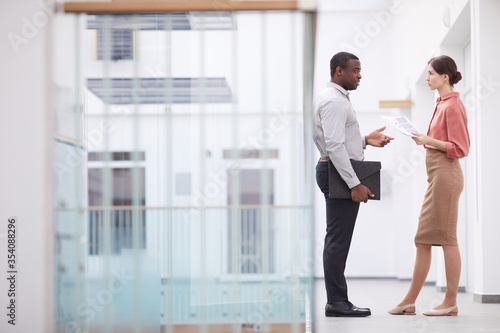 Full length side view portrait of successful African-American businessman talking to young woman while standing at balcony in office building interior, copy space photo