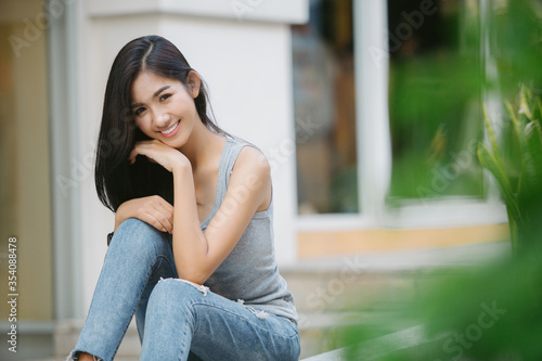 Summer sunny lifestyle fashion portrait of young stylish hipster Asia woman sitting on the street, wearing cute trendy outfit