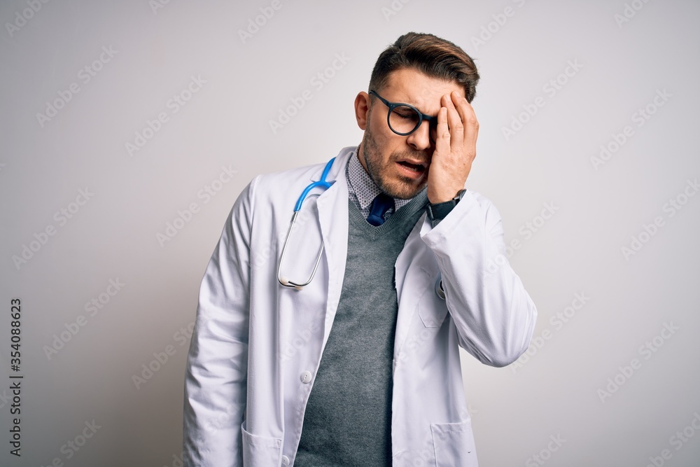Young doctor man with blue eyes wearing medical coat and stethoscope over isolated background Yawning tired covering half face, eye and mouth with hand. Face hurts in pain. Young doctor man with blue eyes wearing medical coat and stethoscope over isolated background Yawning tired covering half face, eye and mouth with hand. Face hurts in pain.