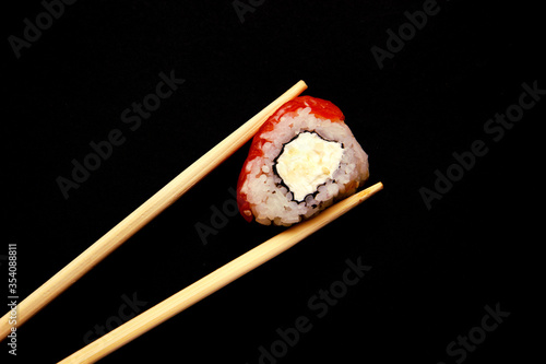 hand holds a roll with red fish of chopsticks, black background.