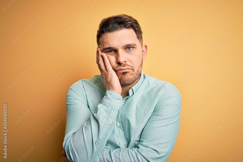 Young business man with blue eyes wearing elegant green shirt over yellow background thinking looking tired and bored with depression problems with crossed arms. Young business man with blue eyes wearing elegant green shirt over yellow background thinking looking tired and bored with depression problems with crossed arms.