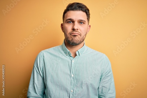 Young business man with blue eyes wearing elegant green shirt over yellow background depressed and worry for distress, crying angry and afraid. Sad expression.
