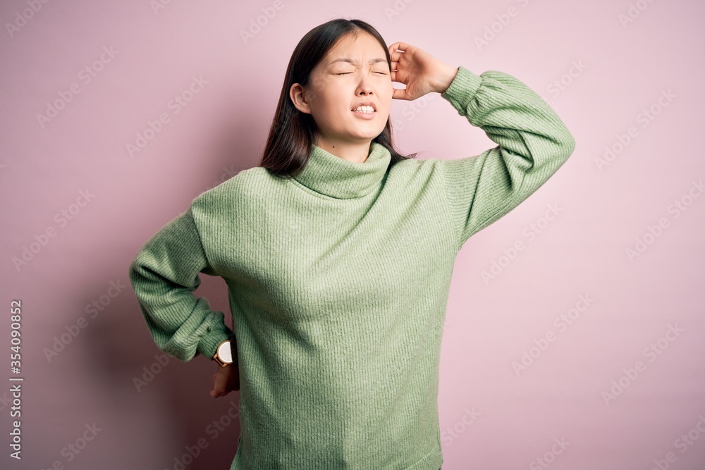 Young beautiful asian woman wearing green winter sweater over pink solated background stretching back, tired and relaxed, sleepy and yawning for early morning Young beautiful asian woman wearing green winter sweater over pink solated background stretching back, tired and relaxed, sleepy and yawning for early morning