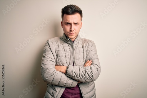 Young handsome caucasian man wearing casual winter jacket standing over isolated background skeptic and nervous, disapproving expression on face with crossed arms. Negative person.