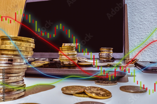 A tower made by coins on a laptop and other coins around it. Finance, bank , money themes. And trading and finance charts on the top.