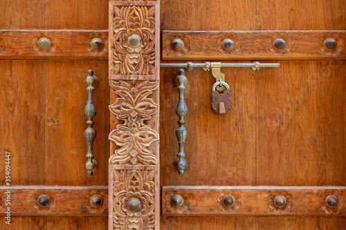 Detail of brown wooden door with carvings and metal handles in old town of Al Mudairib, Oman
