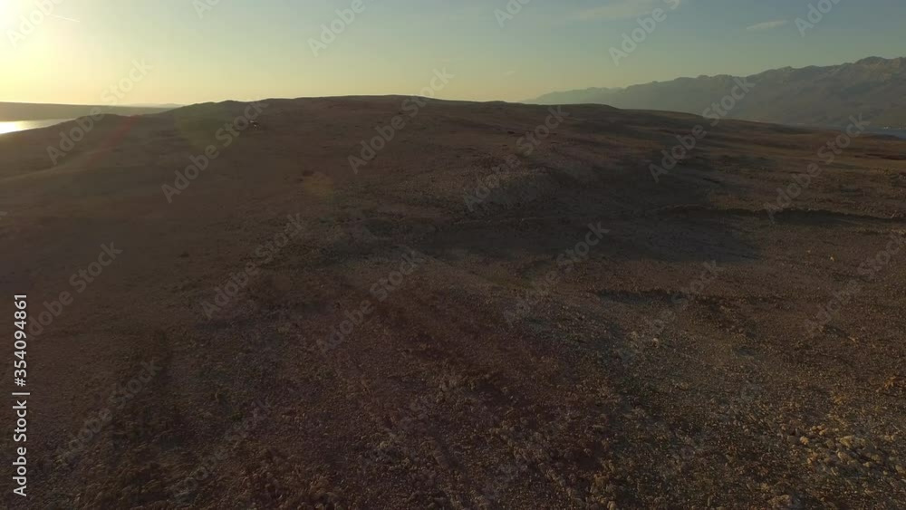 Aerial shot of rocky landscape with sheep against sky, drone ascending while flying forward towards mountains during sunset - Razanac, Croatia Aerial shot of rocky landscape with sheep against sky, drone ascending while flying forward towards mountains during sunset - Razanac, Croatia