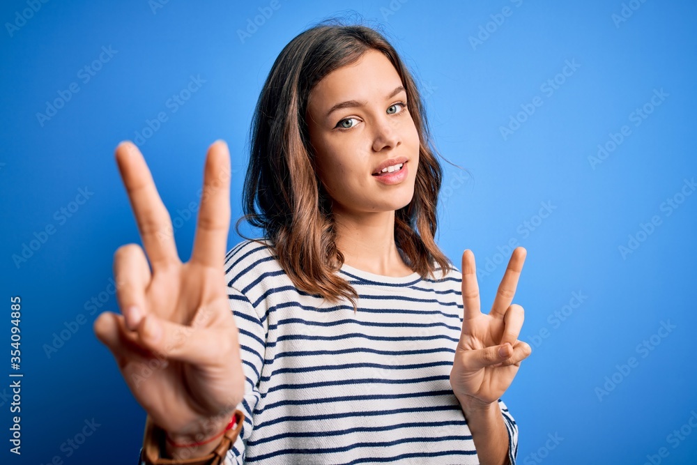Young beautiful blonde girl wearing casual sweater standing over blue isolated background smiling looking to the camera showing fingers doing victory sign. Number two. Young beautiful blonde girl wearing casual sweater standing over blue isolated background smiling looking to the camera showing fingers doing victory sign. Number two.