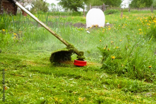 a man mows the lawn with a gas mower with a fishing line