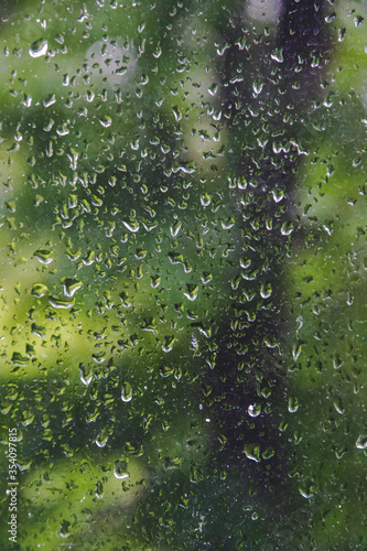 Textured pattern of rain drops on the window and green background. Close up picture of water drops background. Spring season with rainy days. 