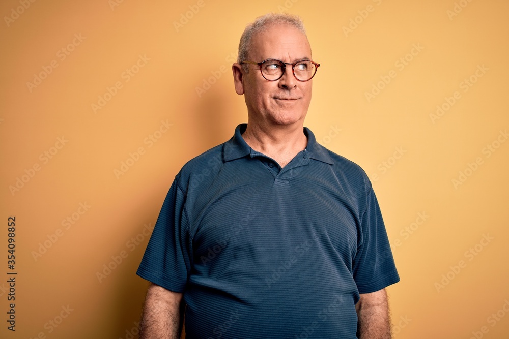 Middle age handsome hoary man wearing casual polo and glasses over yellow background smiling looking to the side and staring away thinking. Middle age handsome hoary man wearing casual polo and glasses over yellow background smiling looking to the side and staring away thinking.