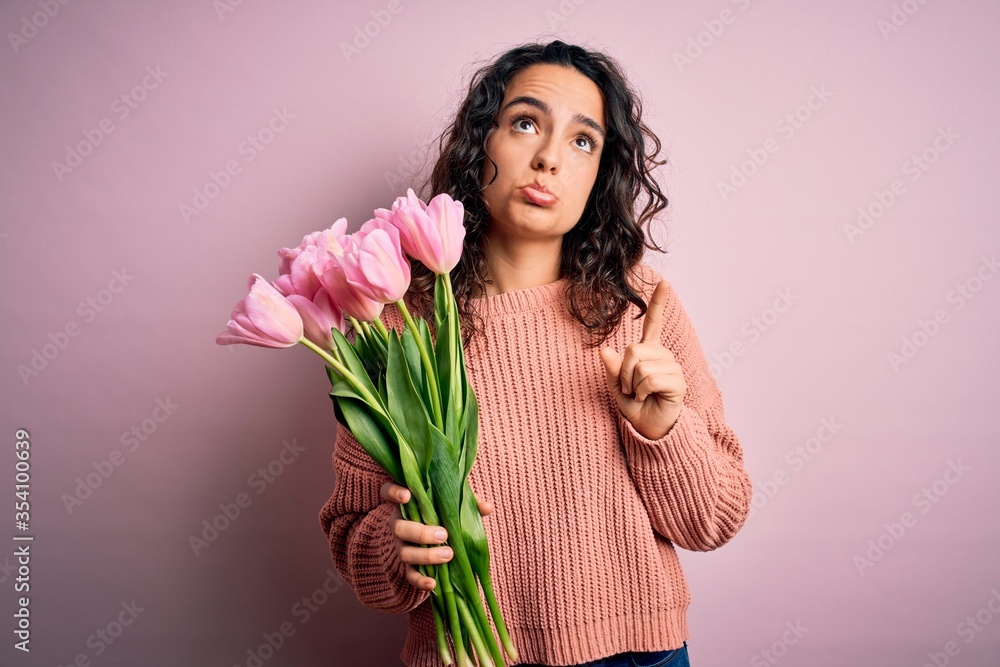 Young beautiful romantic woman with curly hair holding bouquet of pink tulips Pointing up looking sad and upset, indicating direction with fingers, unhappy and depressed. Young beautiful romantic woman with curly hair holding bouquet of pink tulips Pointing up looking sad and upset, indicating direction with fingers, unhappy and depressed.