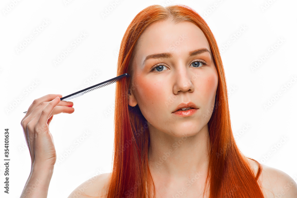 close beauty portrait of a red-haired girl with a clean face who combs her hair with a black comb. Isolated on a white background.