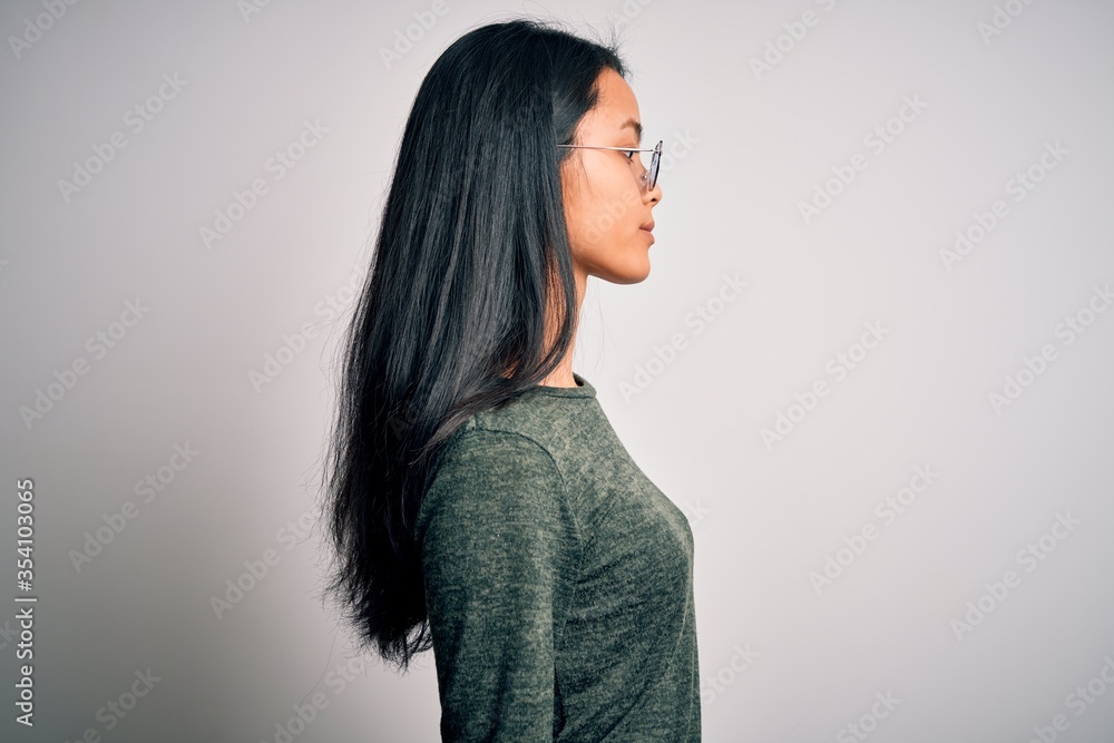 Young beautiful chinese woman wearing glasses and t-shirt over isolated white background looking to side, relax profile pose with natural face with confident smile. Young beautiful chinese woman wearing glasses and t-shirt over isolated white background looking to side, relax profile pose with natural face with confident smile.
