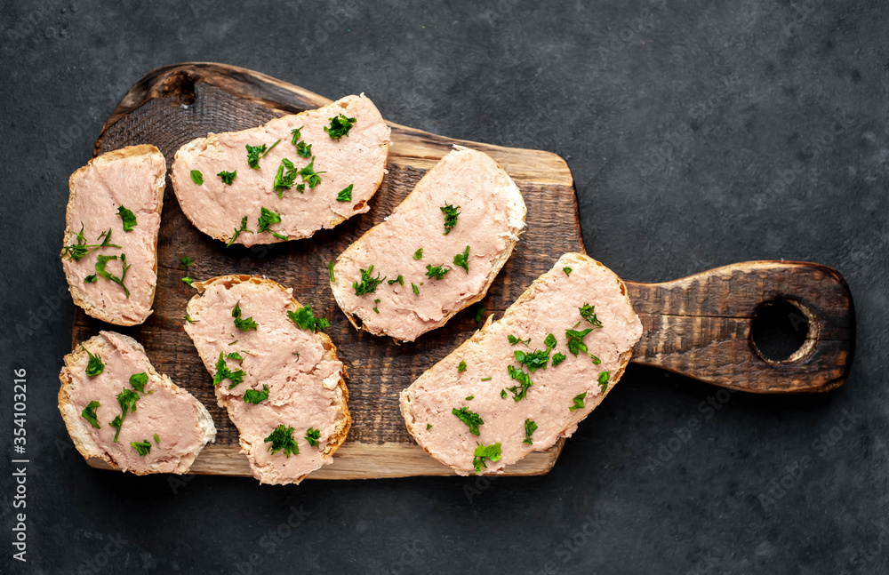 Fototapeta premium Chicken pate on toast with fresh parsley on a cutting board on a stone background