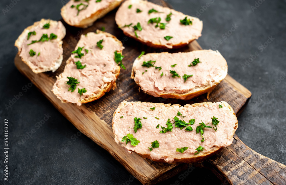 Chicken pate on toast with fresh parsley on a cutting board on a stone background
Chicken pate on toast with fresh parsley on a cutting board on a stone background