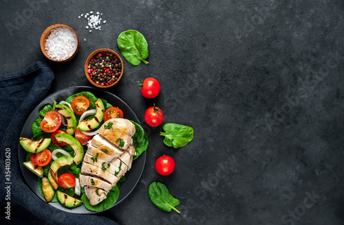 Grilled chicken breast and grilled avocado salad with cherry tomatoes, spinach, in a black plate on a stone background with copy space for your text