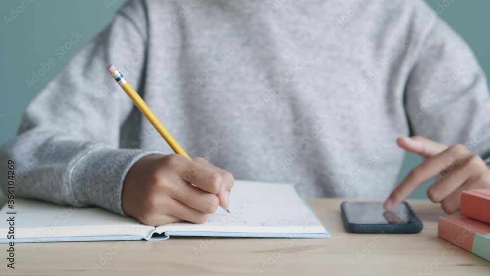 Hand of Asian little girl is writ homework and using smartphone at home Hand of Asian little girl is writ homework and using smartphone at home