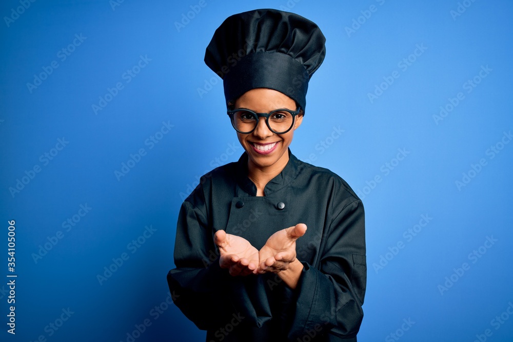 Young african american chef woman wearing cooker uniform and hat over blue background Smiling with hands palms together receiving or giving gesture. Hold and protection Young african american chef woman wearing cooker uniform and hat over blue background Smiling with hands palms together receiving or giving gesture. Hold and protection