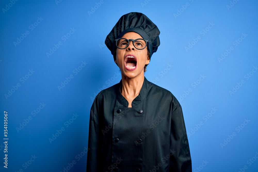 Young african american chef woman wearing cooker uniform and hat over blue background angry and mad screaming frustrated and furious, shouting with anger. Rage and aggressive concept. Young african american chef woman wearing cooker uniform and hat over blue background angry and mad screaming frustrated and furious, shouting with anger. Rage and aggressive concept.