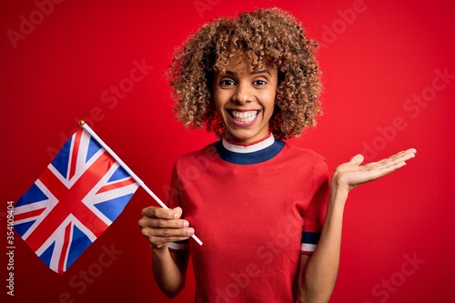 Young african american curly woman holding uk flag celebrating brexit referendum very happy and excited, winner expression celebrating victory screaming with big smile and raised hands