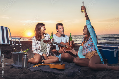 Group of friends with guitar having fun on the beach at sunset. © Mediteraneo