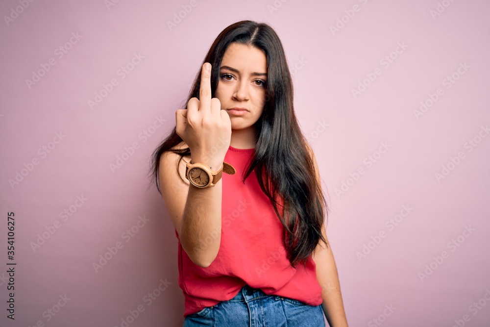 Young brunette woman wearing casual summer shirt over pink isolated background Showing middle finger, impolite and rude fuck off expression Young brunette woman wearing casual summer shirt over pink isolated background Showing middle finger, impolite and rude fuck off expression
