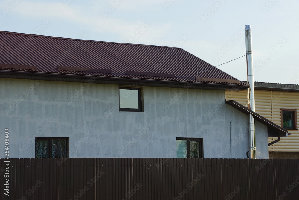  private gray house with windows under a tiled roof against a sky behind a fence 