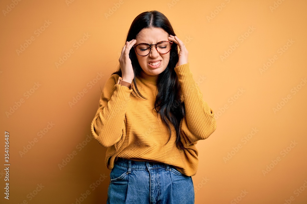 Young brunette woman wearing glasses and casual sweater over yellow isolated background with hand on headache because stress. Suffering migraine.