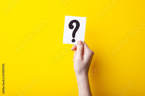 Woman holding card with question mark on color background. Paper note with question mark or sign against yellow background.  Ask or business concept photo