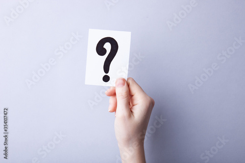 Woman holding card with question mark on color background. Paper note with question mark or sign against grey background. Ask or business concept