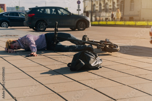 A young man after an accident lying on the road near a scooter