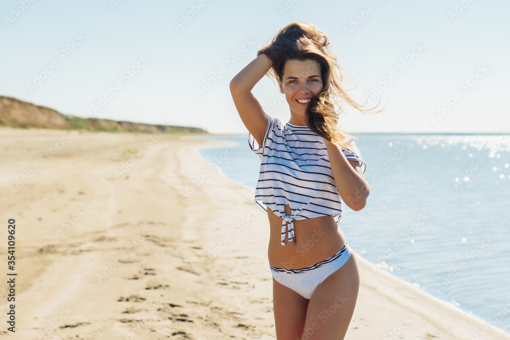 Young attractive brunette woman in white striped shirt and thong  enjoying the summer with sea on background