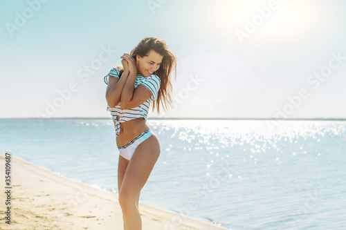 Young attractive brunette woman in white striped shirt and thong enjoying the summer with sea on background