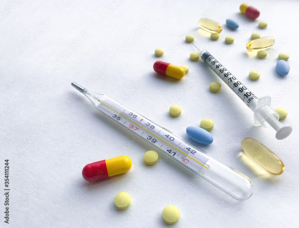 A lot of colorful pills, syringe, thermometer - on the right, against a white textured rough sheet of paper with space for text A lot of colorful pills, syringe, thermometer - on the right, against a white textured rough sheet of paper with space for text