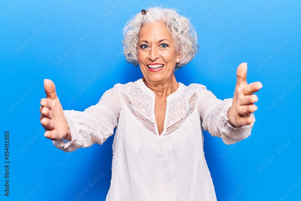Senior grey-haired woman wearing casual clothes looking at the camera smiling with open arms for hug. cheerful expression embracing happiness. Senior grey-haired woman wearing casual clothes looking at the camera smiling with open arms for hug. cheerful expression embracing happiness.