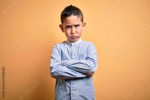Young little boy kid wearing elegant shirt standing over yellow isolated background skeptic and nervous, disapproving expression on face with crossed arms. Negative person.