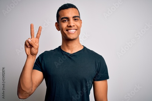 Young handsome african american man wearing casual t-shirt standing over white background showing and pointing up with fingers number two while smiling confident and happy. © Krakenimages.com