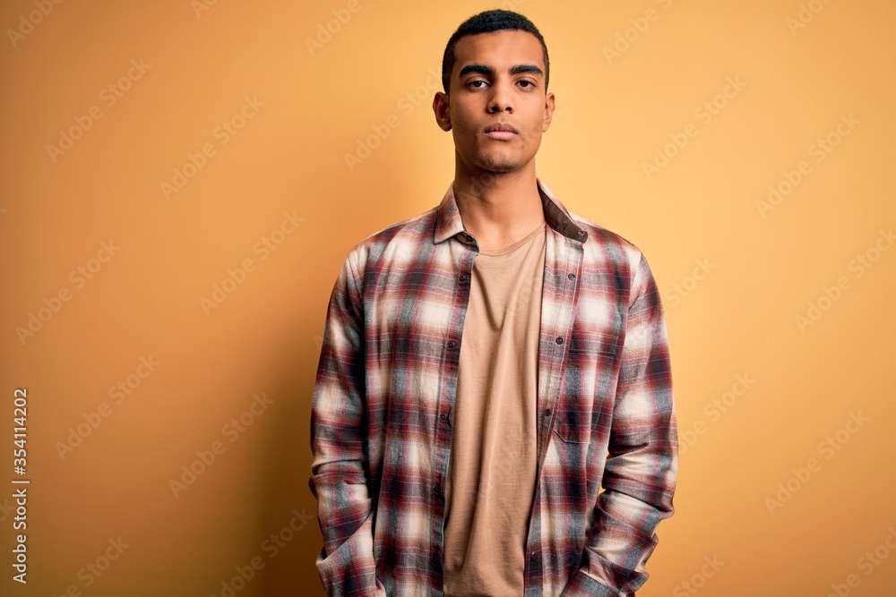 Young handsome african american man wearing casual shirt standing over yellow background Relaxed with serious expression on face. Simple and natural looking at the camera. Young handsome african american man wearing casual shirt standing over yellow background Relaxed with serious expression on face. Simple and natural looking at the camera.