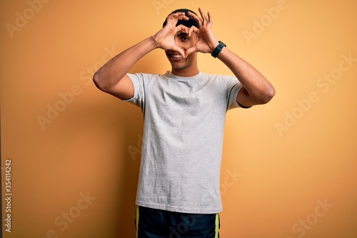 Handsome african american sportsman doing sport wearing sportswear over yellow background Doing heart shape with hand and fingers smiling looking through sign