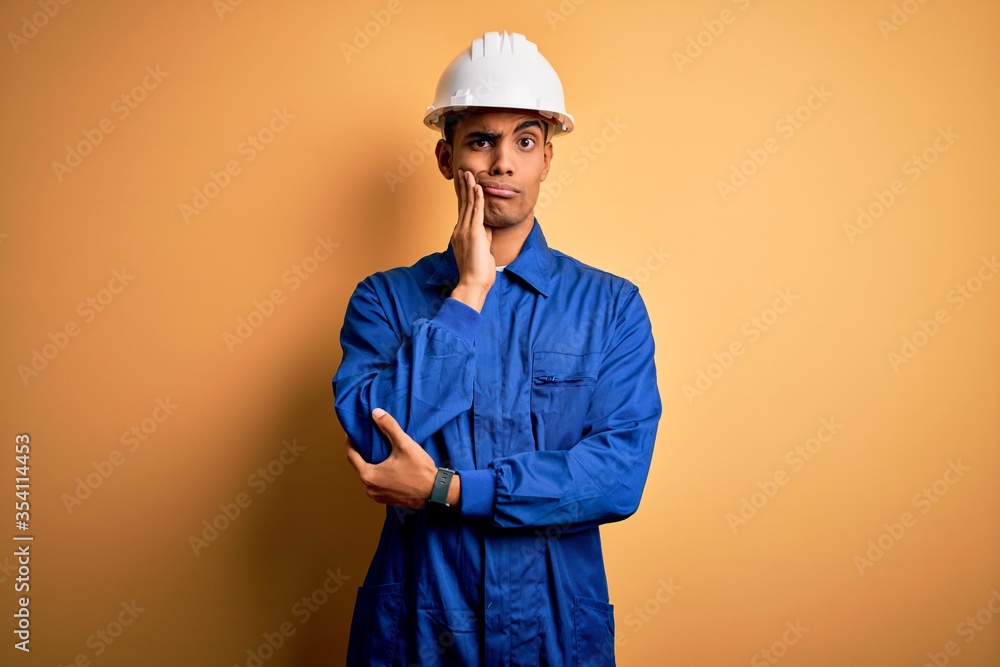 Young handsome african american worker man wearing blue uniform and security helmet thinking looking tired and bored with depression problems with crossed arms.
