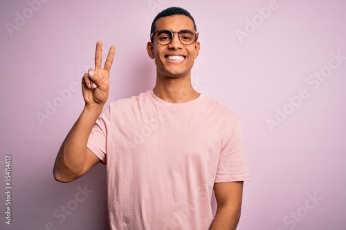 Handsome african american man wearing casual t-shirt and glasses over pink background showing and pointing up with fingers number two while smiling confident and happy. © Krakenimages.com
