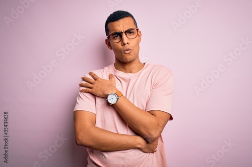 Handsome african american man wearing casual t-shirt and glasses over pink background shaking and freezing for winter cold with sad and shock expression on face