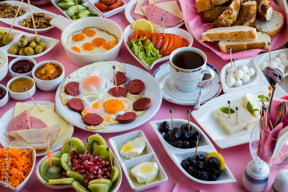 Traditional Turkish spreading breakfast with fry quail eggs and sausage egg on the middle of table with a cup of tea.Used completely white porcelain breakfast set.Pink ground and large view. Traditional Turkish spreading breakfast with fry quail eggs and sausage egg on the middle of table with a cup of tea.Used completely white porcelain breakfast set.Pink ground and large view.