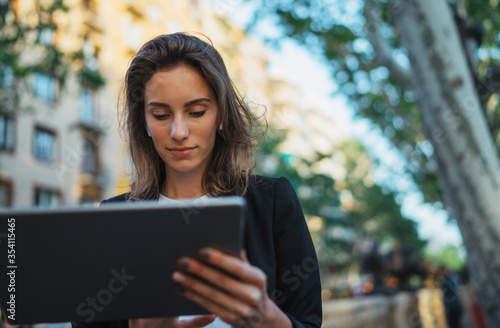 Young pretty spanish woman working tablet in city centre. Portrait of young woman enjoying music in earphones chilling in park, female freelancer working outside using modern device to communicate