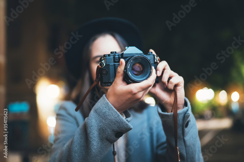 Photographer tourist girl with retro camera take photo on background bokeh light in evening city, Blogger photoshoot photo hobby