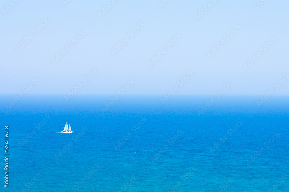 Beautiful seascape with calm blue Mediterranian sea in mist and boat, touristic season, vacation on sunny islands